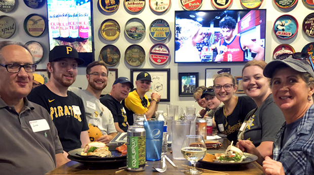 A group of La Roche University alumni seated at a table with food and drinks at a happy hour event before a Pittsburgh Pirates game.