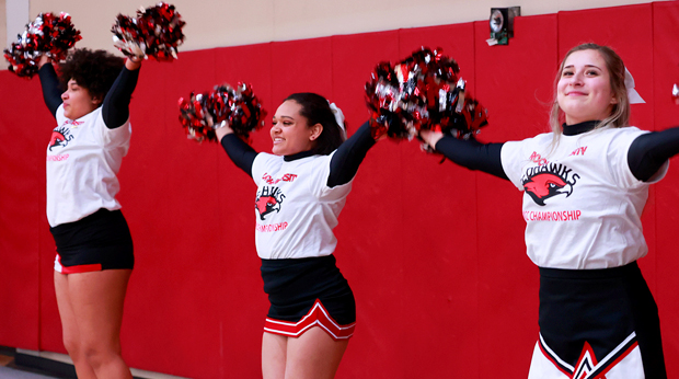 Three La Roche University cheerleaders cheering at a basketball game.