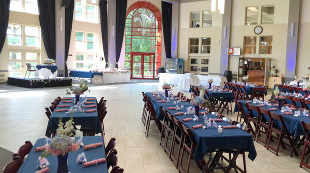 The Zappala Campus Center Square at La Roche University with tables set up for a wedding. Tables have flower centerpieces, tablecloths, favors, and silverware wrapped in cloth napkins. 