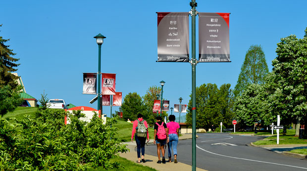 Three La Roche University students walk on the sidewalk  from the parking lot to the Zappala Campus Center building on a summer day.