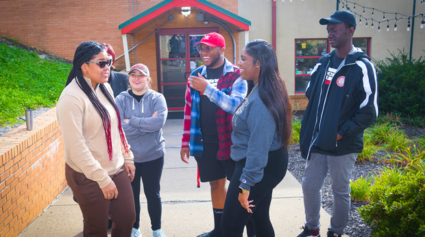 Five La Roche University students laugh together in the courtyard between Wright Library and the Zappala Campus Center building.