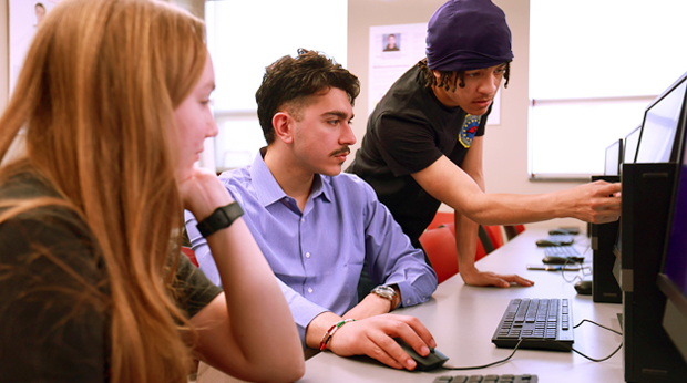 Three La Roche University students look at a project together on a computer in the cybersecurity lab. One student points to the computer screen.