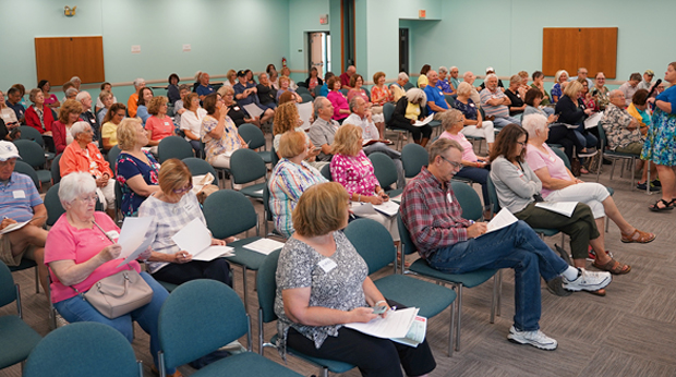 A crowd of the Adventures in Lifelong Learning members La Roche University are seated in a conference room, listening the program director talk in front of the room.