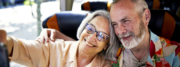 Two people sit together and pose for a photo. One of them holds a phone up in front of them to take a selfie.