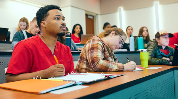 Students sit taking notes and listening to a lecture in the auditorium classroom at La Roche University.