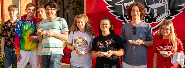 A group of La Roche University students stand in front of food truck. Some of them hold bowls of ice cream. 