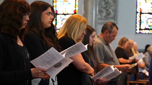 Students and their families stand holding programs during a Baccalaureate Mass in the Motherhouse Chapel. 